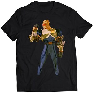 May include: Black t-shirt featuring a cartoon illustration of a character with blond hair, red goggles, and a blue and yellow suit. The character is holding a weapon in their right hand.