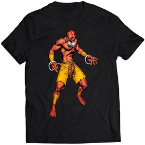 Könnte beinhalten: Schwarzes T-Shirt mit einem rotköpfigen Charakter, der gelbe Shorts und eine Halskette mit Totenköpfen trägt. Der Charakter ist in einer Kampfpose mit erhobenen Armen dargestellt.