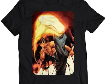 May include: Black t-shirt featuring a graphic of a man in a fighting pose with a fiery orange and yellow aura around his foot.