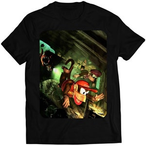 Puede incluir: Una camiseta negra con un estampado gráfico de tres monos de la serie de videojuegos Donkey Kong. Los monos están en un entorno oscuro y selvático. El mono principal lleva un sombrero rojo y sostiene un arma. Los otros dos monos están detrás de él. La camiseta es una gran manera de mostrar tu amor por la franquicia Donkey Kong.