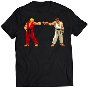 May include: Black t-shirt featuring a pixelated graphic of two characters in fighting stances, one in red and the other in white. The characters are fist-bumping. The design is centered on the shirt.