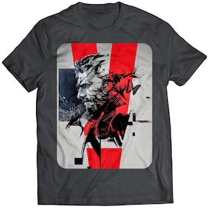 May include: A dark grey t-shirt featuring a graphic print of a character from the video game Metal Gear Solid. The graphic is in black, white and red, and depicts the character's face with a stylised 'V' in the background.