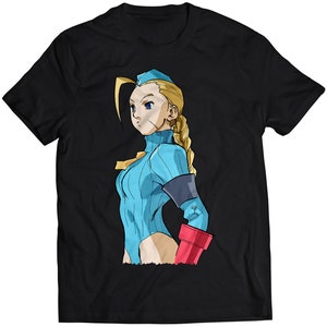 Op de afbeelding: Zwart T-shirt met een afbeelding van een vrouwelijk personage met blond haar, dat een blauwe jumpsuit en een rode handschoen draagt.