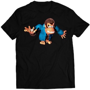 Puede incluir: Camiseta negra con una imagen de dibujos animados de Donkey Kong con un traje azul y un anillo de oro en el dedo.
