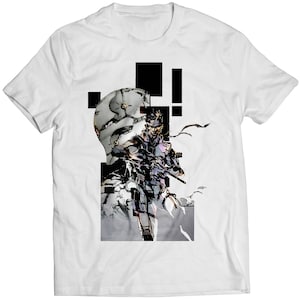 Op de afbeelding: Wit T-shirt met een zwart-witte grafische print van een personage uit een videogame. Het personage houdt een pistool vast en draagt ​​een bandana. De grafiek is omgeven door zwarte rechthoeken.