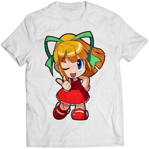 Puede incluir: Una camiseta blanca con una imagen de dibujos animados de una niña con cabello rubio, vistiendo un vestido rojo y lazos verdes. Ella está guiñando un ojo y levantando dos dedos en señal de paz.