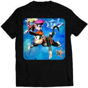 Puede incluir: Una camiseta negra con un gráfico colorido de un mono, una niña y una raya nadando bajo el agua. El gráfico está rodeado de burbujas y una estrella de mar.