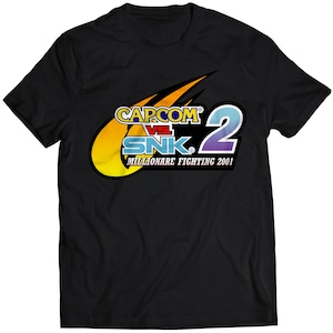 Könnte beinhalten: Schwarzes T-Shirt mit einer gelben, blauen und violetten Grafik des Capcom vs. SNK 2: Millionaire Fighting 2001 Logos.