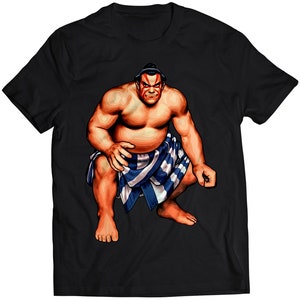 Könnte beinhalten: Ein schwarzes T-Shirt mit einem Grafikdruck eines muskulösen Sumo-Ringers, der einen blau-weiß gemusterten Lendenschurz trägt. Der Ringer hat ein rotes und weißes Gesichtsbemalungsmuster.