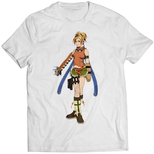 May include: White t-shirt featuring a cartoon illustration of a female character with blonde hair, wearing a brown and orange outfit, holding a blue and orange weapon.