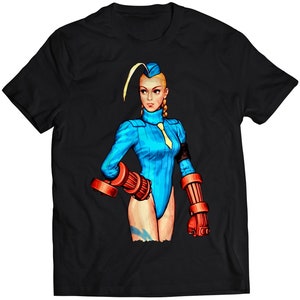 Könnte beinhalten: Ein schwarzes T-Shirt mit einer bunten Illustration einer weiblichen Figur aus einem Videospiel. Sie trägt ein blaues und weißes Outfit und hält eine rote und orangefarbene Waffe.