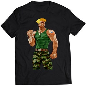 May include: Black t-shirt featuring a muscular character in a green tank top and camouflage pants. The character has blonde hair and an American flag tattoo on his arm. The design is a stylized illustration.