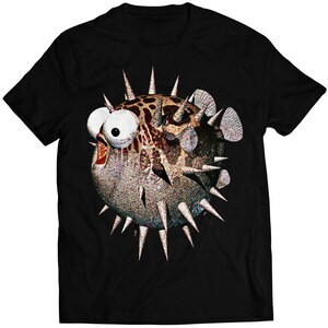 Puede incluir: Camiseta negra con un gráfico de un pez globo de dibujos animados con ojos grandes y aletas espinosas.