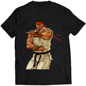 Könnte beinhalten: Schwarzes T-Shirt mit einer Cartoon-Illustration eines Kampfsportlers in einem weißen Gi, rotem Stirnband und schwarzem Gürtel. Der Kämpfer befindet sich in Kampfstellung mit erhobenen Armen.