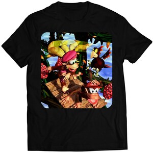 Puede incluir: Una camiseta negra con un gráfico colorido de dos monos y un pájaro en una plataforma de madera en un entorno de jungla. Los monos llevan sombreros y el pájaro es rojo y azul.