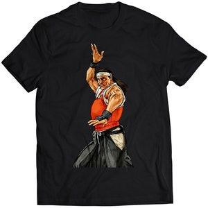 Könnte beinhalten: Ein schwarzes T-Shirt mit einer bunten Illustration eines Kampfsportlers in einem rot-weißen Outfit. Der Kämpfer befindet sich in Kampfstellung mit einem erhobenen Arm.
