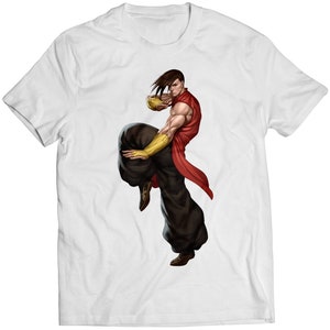 May include: White t-shirt featuring a dynamic illustration of a martial artist in a fighting stance. The character is depicted with a red top, black pants, and gold arm guards, holding a golden object. The artwork is detailed and vibrant.