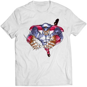 May include: White t-shirt with a colorful illustration of a cartoon character wearing a blue and white uniform and a red and white cape. The character is flying through the air with their fists clenched.