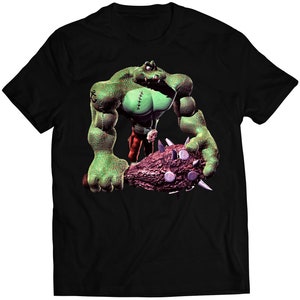 Puede incluir: Camiseta negra con un monstruo verde sosteniendo un garrote con pinchos. El monstruo tiene puntos de sutura en el pecho y lleva pantalones rojos.