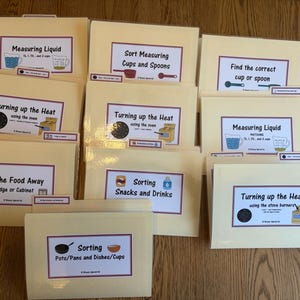 May include: A collection of light yellow file folders with various labels. The labels include text such as "Measuring Liquid", "Turning up the Heat", and "Sorting Snacks and Drinks". Each folder has a white label with black text and colorful illustrations.