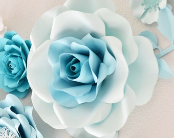 Op de afbeelding: Een grote, lichtblauwe papieren bloem met een wit centrum. De bloem heeft meerdere lagen bloemblaadjes en is een populaire decoratie voor bruiloften en feestjes.