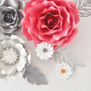 Op de afbeelding: Een verzameling papieren bloemen in tinten grijs, wit en roze. De bloemen zijn gerangschikt op een witte achtergrond en omvatten rozen en madeliefjes.