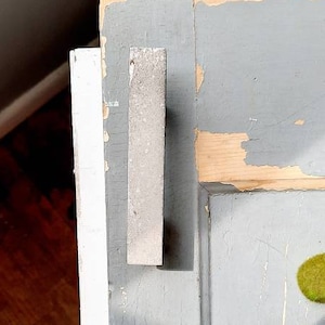 May include: Close-up of a gray cabinet door with a silver metal cabinet pull. The door has a distressed finish with visible wood grain.