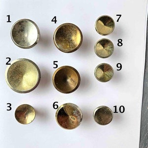 May include: Ten different styles of round, gold-toned cabinet knobs with varying finishes. The knobs are numbered 1 through 10.