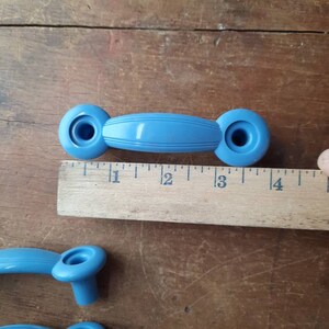 Puede incluir: Tres pomos de armario de pl&aacute;stico azul con forma ovalada redondeada. Los pomos tienen un agujero en el centro y una cresta elevada alrededor del borde. Los pomos miden aproximadamente 5 cm de largo.
