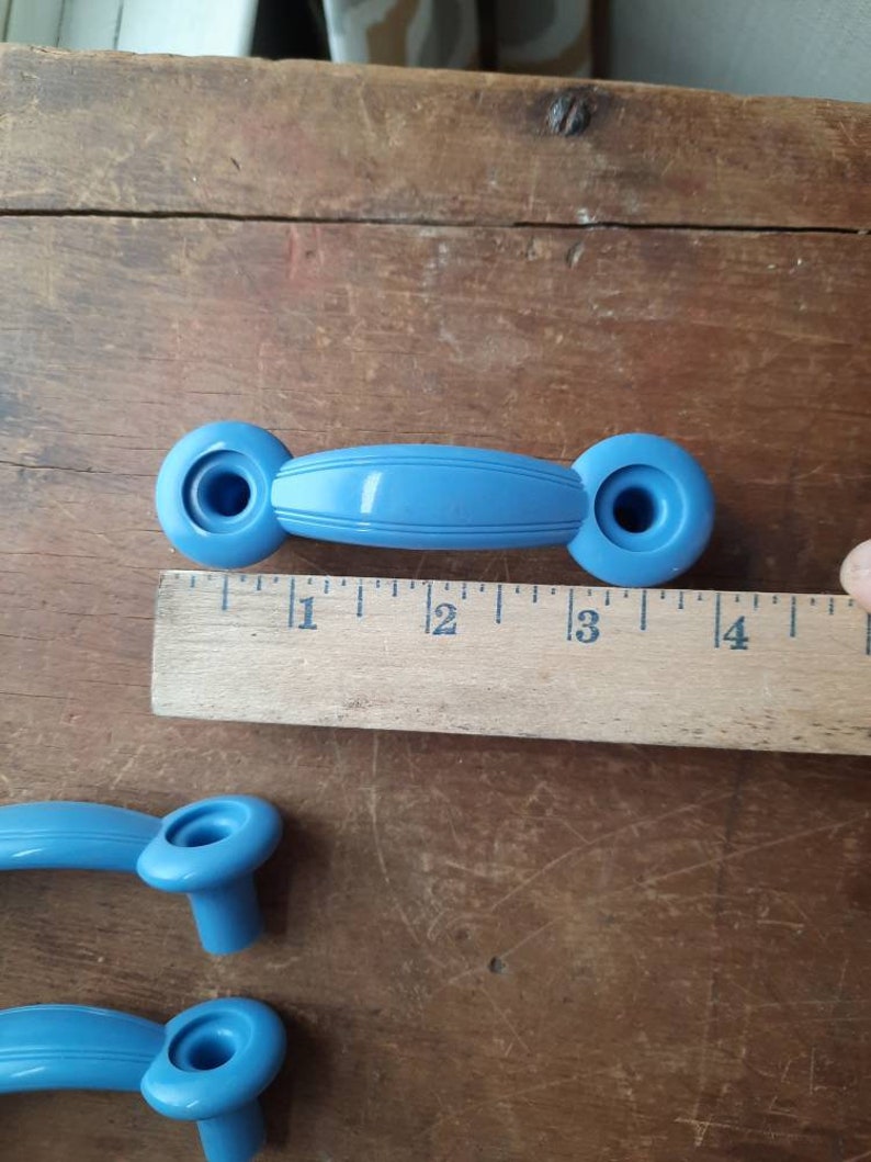 Puede incluir: Tres pomos de armario de pl&aacute;stico azul con forma ovalada redondeada. Los pomos tienen un agujero en el centro y una cresta elevada alrededor del borde. Los pomos miden aproximadamente 5 cm de largo.