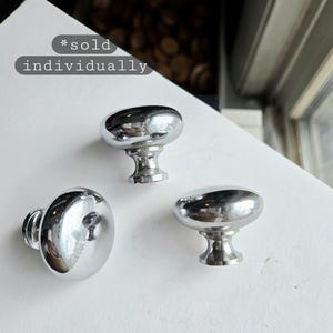 May include: Three shiny chrome cabinet knobs with an oval design. The knobs are displayed on a white surface. The text "*sold individually" is in the background.