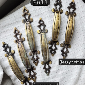 May include: Five elongated metal drawer pulls with ornate, scroll-like ends and textured central panels. The hardware features varying degrees of aged brass finish, with labels indicating 'Pull', '(less patina)', and '(more patina)' on the image.