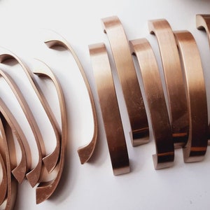 May include: A set of ten gold-toned cabinet pulls with a curved design. The pulls are arranged in a staggered pattern on a white surface.