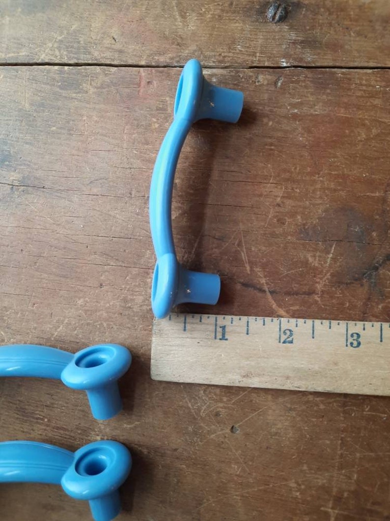 Puede incluir: Tres tiradores de puerta de armario de pl&aacute;stico azul. Los tiradores son curvos y tienen un extremo redondeado. Los tiradores miden aproximadamente 7,6 cm de largo.