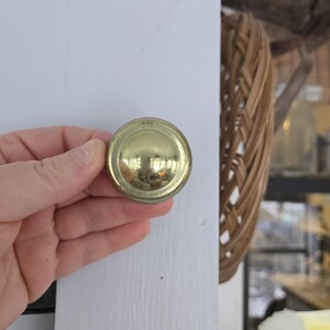 May include: A gold-toned round cabinet knob with a raised, slightly domed center.