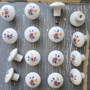May include: A set of 15 white ceramic drawer knobs with a floral design. The knobs feature a variety of pink, yellow, and blue flowers.