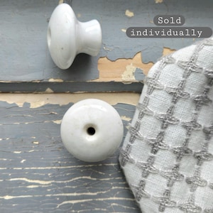May include: Two white ceramic knobs with a smooth, glossy finish. One knob is shown from the side, and the other is shown from the top, revealing a central hole. The text "Sold individually" is visible in the upper right corner of the image.
