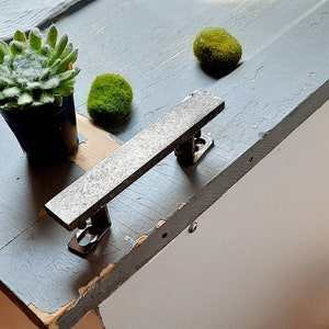 May include: A gray wooden box with a metal handle. The box is painted a light gray and has a white interior. The handle is made of metal and has a rough texture. The box is sitting on a wooden floor.