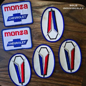 May include: Five vintage embroidered patches. Two patches are blue and white with the text "monza CHEVROLET". Three patches are white with a blue and red emblem that resembles a stylized coffin.