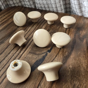 以下が含まれることがあります： 滑らかで丸みを帯びた表面を持つ、クリーム色のセラミック製のキャビネットノブが9個あります。ノブの中央には、取り付け用の小さな穴があります。