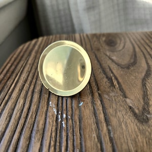 May include: A round, gold-colored metal knob with a smooth, shiny surface.