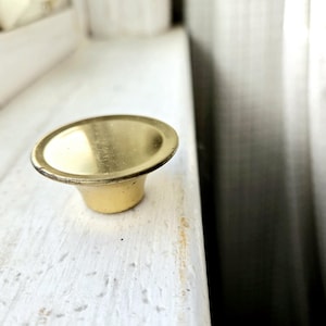 May include: A gold-colored metal knob with a rounded top and a slightly flared base.