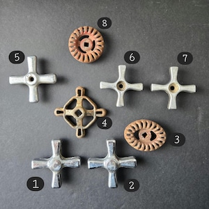 May include: A collection of vintage faucet handles and parts in various shapes and materials. Includes cross-shaped chrome handles, a handle marked with "C" and "H", and aged, circular and geometric designs in metal.