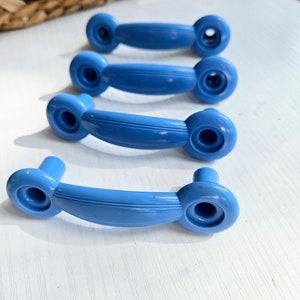 Puede incluir: Cuatro pomos de armario de pl&aacute;stico azul con un dise&ntilde;o redondeado y curvo. Los pomos tienen un acabado liso y brillante.