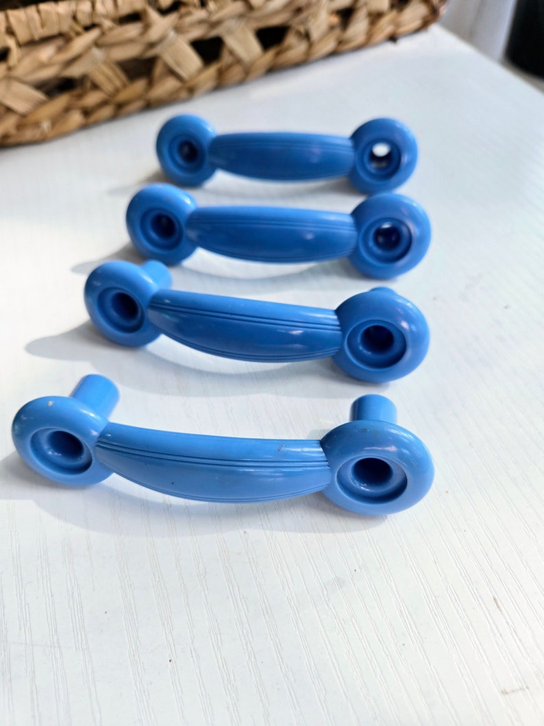 Puede incluir: Cuatro pomos de armario de pl&aacute;stico azul con un dise&ntilde;o redondeado y curvo. Los pomos tienen un acabado liso y brillante.