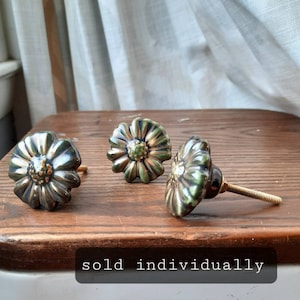 May include: Three ceramic flower-shaped drawer knobs with gold accents. The knobs are green and black with a glossy finish. The knobs are sold individually.