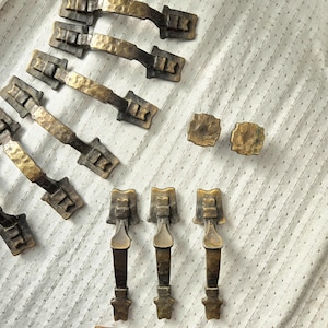 May include: A collection of antique bronze hardware, including drawer pulls and knobs. The drawer pulls have a hammered texture and a dark bronze finish, while the knobs are square. A wooden ruler is in the foreground.