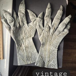 May include: Two gray, textured, monster-like hands with long, pointed fingernails. The hands are detailed with veins and bumps. The word "vintage" is written in a white font on a black oval.