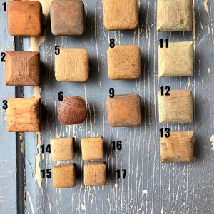 May include: A collection of 17 wooden knobs in various shades of brown, beige, and green. The knobs are arranged in rows on a blue surface with white cracks. The knobs are numbered 1 through 17.