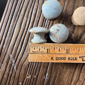 May include: A collection of six vintage blue and white painted wooden knobs. The knobs are round and have a slightly distressed finish. The knobs are arranged on a wooden surface with a ruler that reads "A Good Rule".